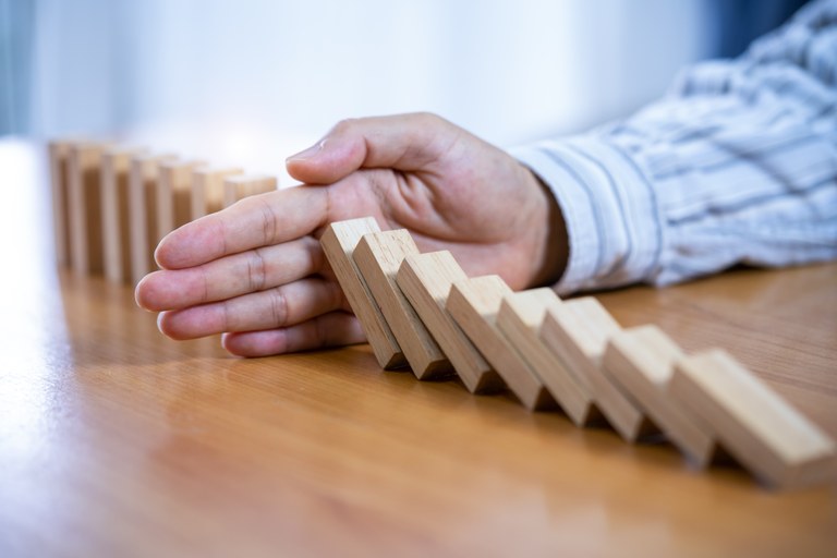 Eine Männerhand stoppt auf halber Länge das Umkippen einer Reihe von Dominosteinen