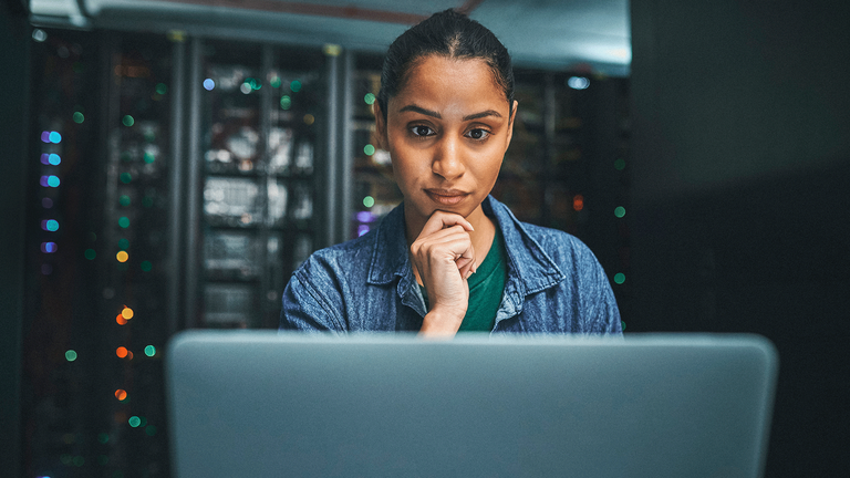 Junge Informatikerin in Serverraum blickt auf den Monitor eines Laptops