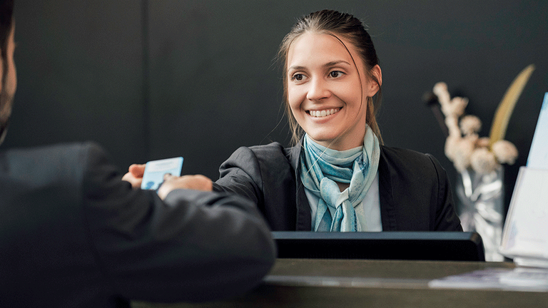 Junge Hotelfachfrau reicht Gast eine Keycard über den Tresen