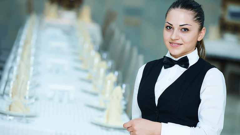 Junge Fachfrau für Restaurants und Veranstaltungsgastronomie vor einer eingedeckten Tafel